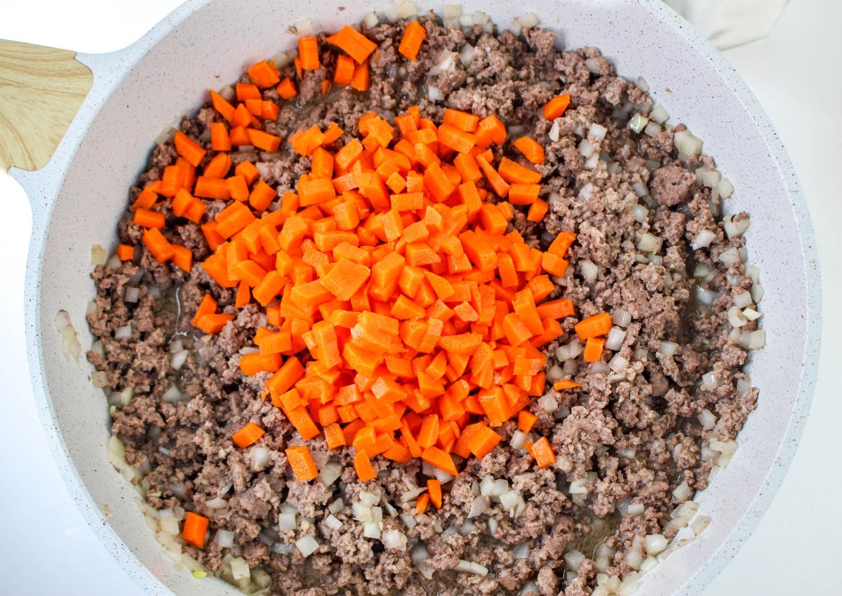 carrots being added to cooked meat in a skillet.