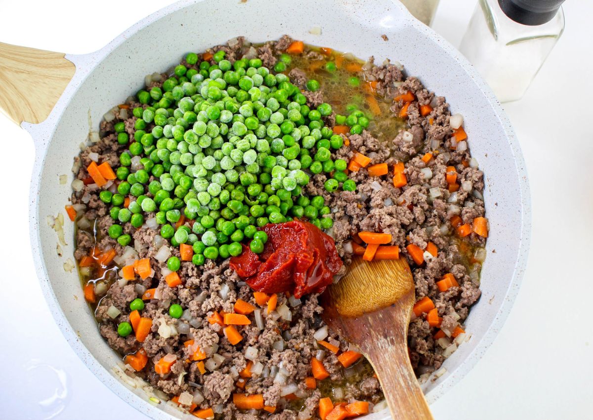 vegetables being added to cooked beef in a large skillet.