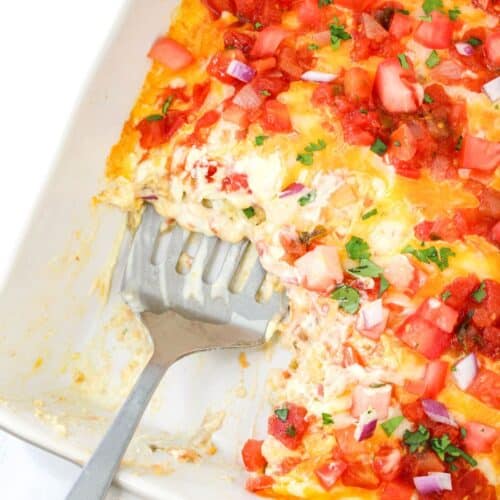 scoop of beef taquito casserole being removed from the casserole dish with a meta spatula.