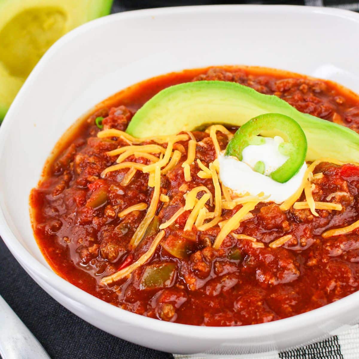 bowl full of no bean chili topped with shredded cheese, sour cream, jalapeno slice, and slice of avocado.