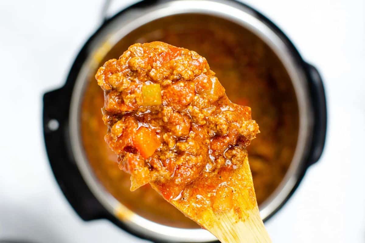 Close-up of a spoon holding a serving of chunky meat and tomato sauce over a pot.