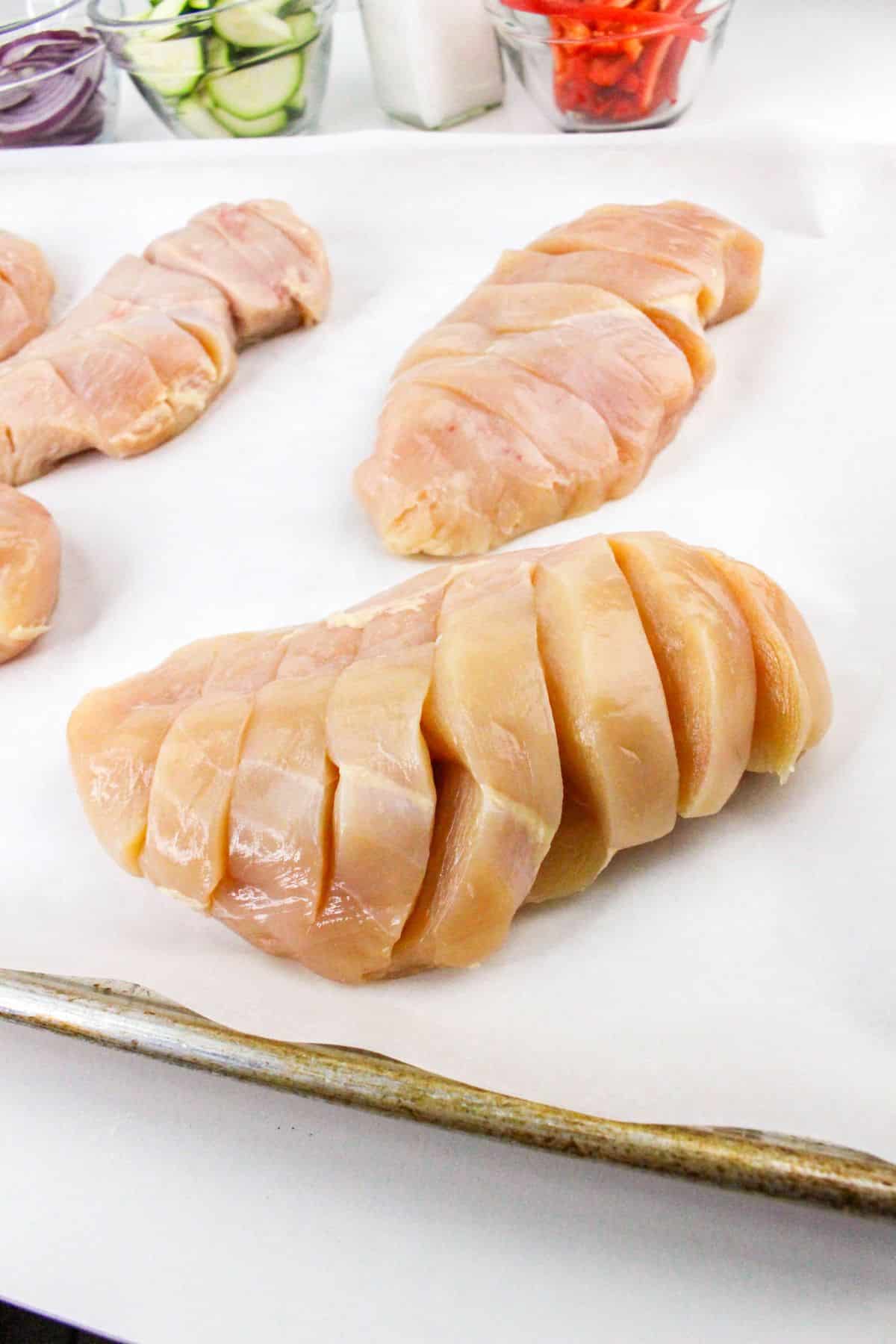 Raw chicken breasts sliced on a baking sheet, ready for seasoning.