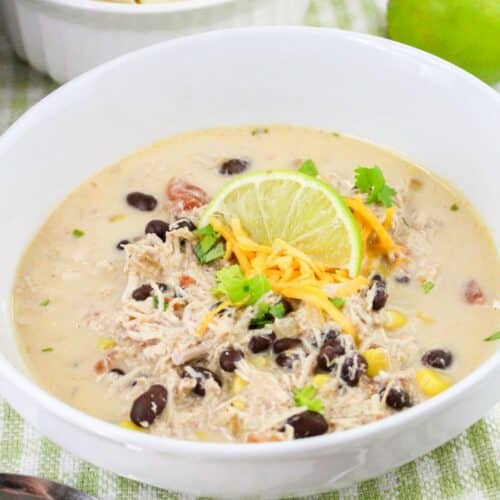 Bowl of chicken tortilla soup topped with black beans, shredded cheese, and a lime slice.