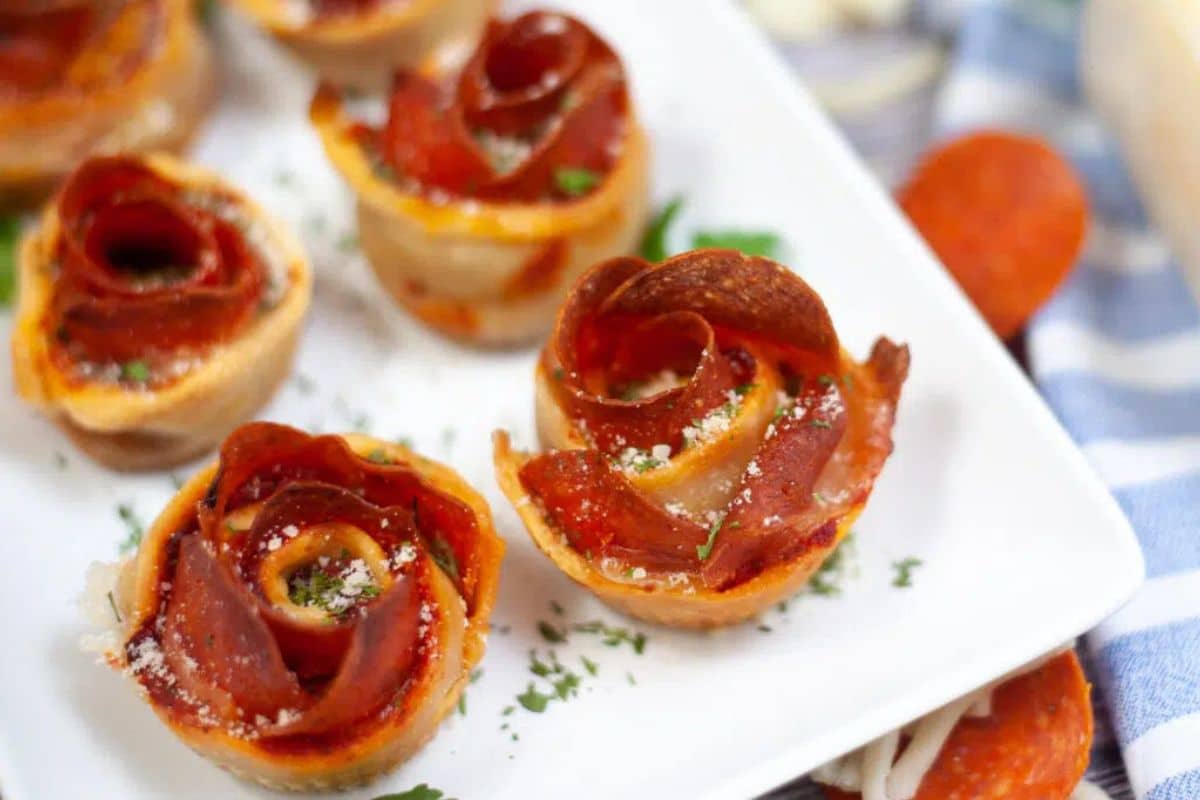 Close-up of pepperoni roses on a white plate, garnished with herbs and grated cheese.