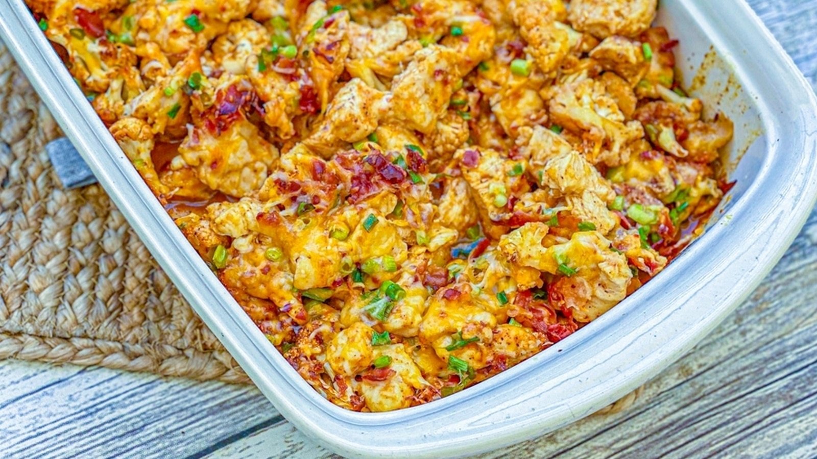 Baked casserole with melted cheese, shredded chicken, and green onions in a rectangular dish on a woven mat.