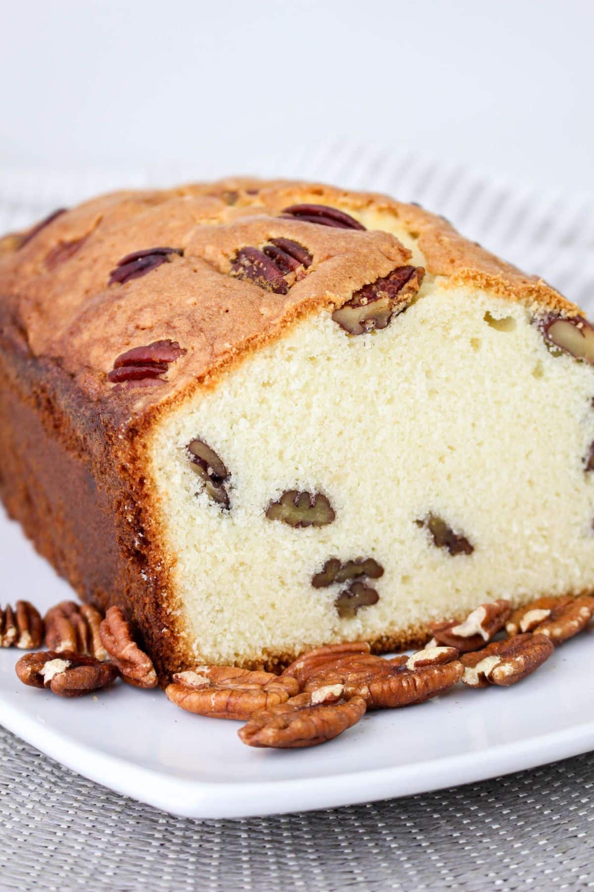 A sliced loaf of pecan bread on a white plate, with whole pecans scattered around.
