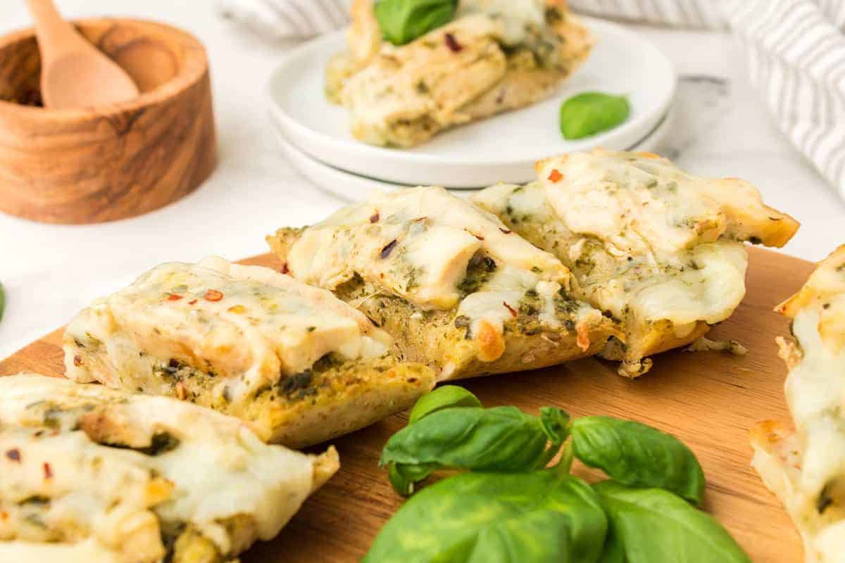 Slices of cheesy bread with herbs on a wooden board, garnished with fresh basil.