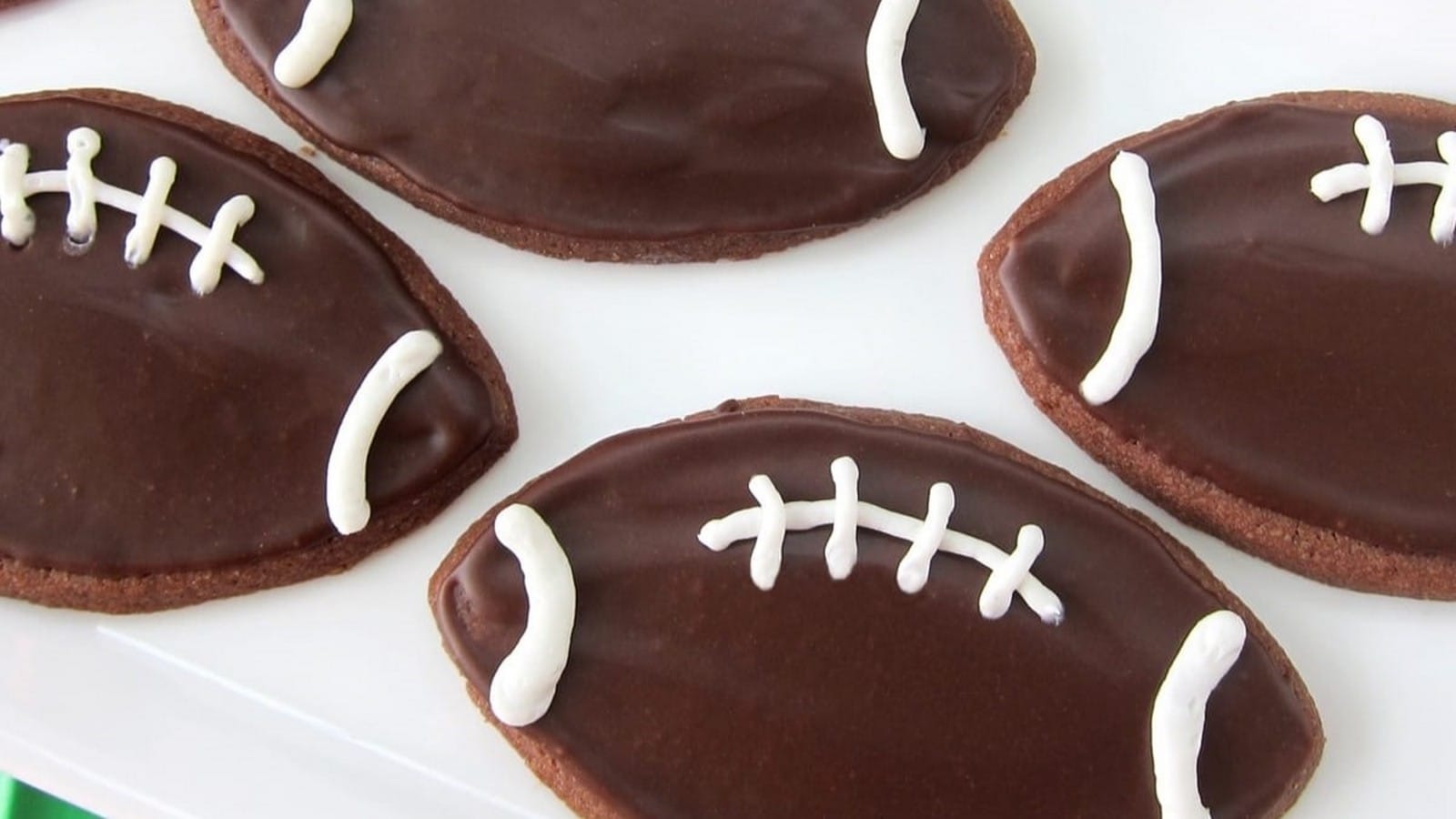 Football-shaped cookies with chocolate icing and white icing laces arranged on a white plate.