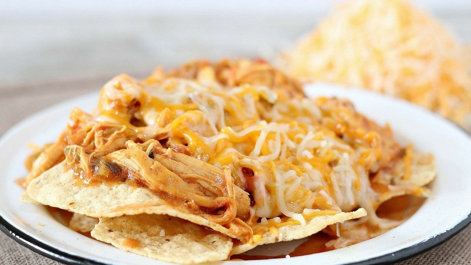 A plate of nachos topped with melted cheese and shredded chicken.