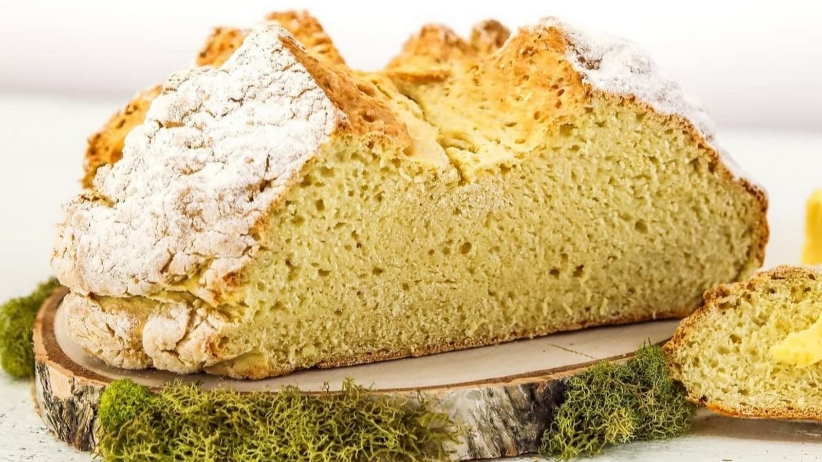 Close-up of a sliced, crusty loaf of soda bread on a wooden board, with a textured golden-brown exterior and a light, airy interior.