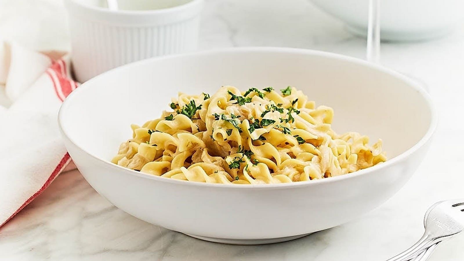 A white bowl filled with fusilli pasta topped with a creamy sauce and garnished with chopped parsley, placed on a marble surface.