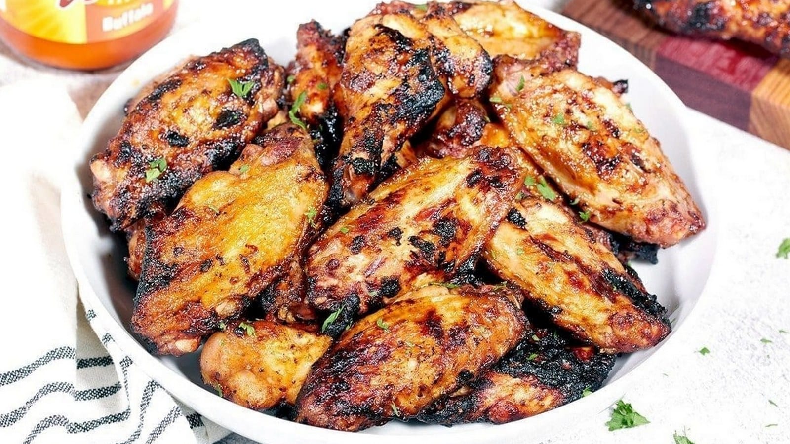 A white bowl filled with grilled buffalo wings, seasoned with herbs and served on a striped cloth.