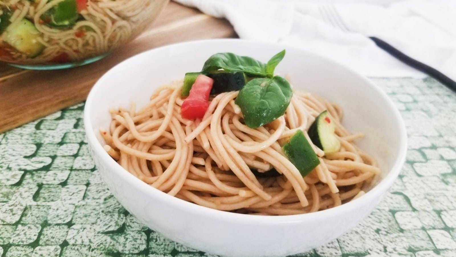 Bowl of noodles with chopped cucumbers and red peppers, garnished with fresh basil.