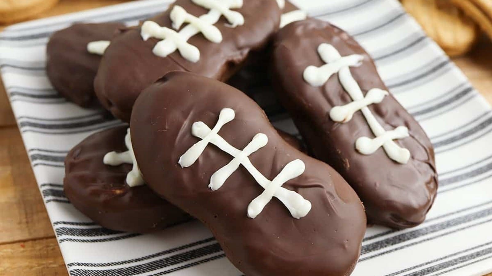 Chocolate-covered cookies decorated to resemble footballs with white icing on a striped plate.