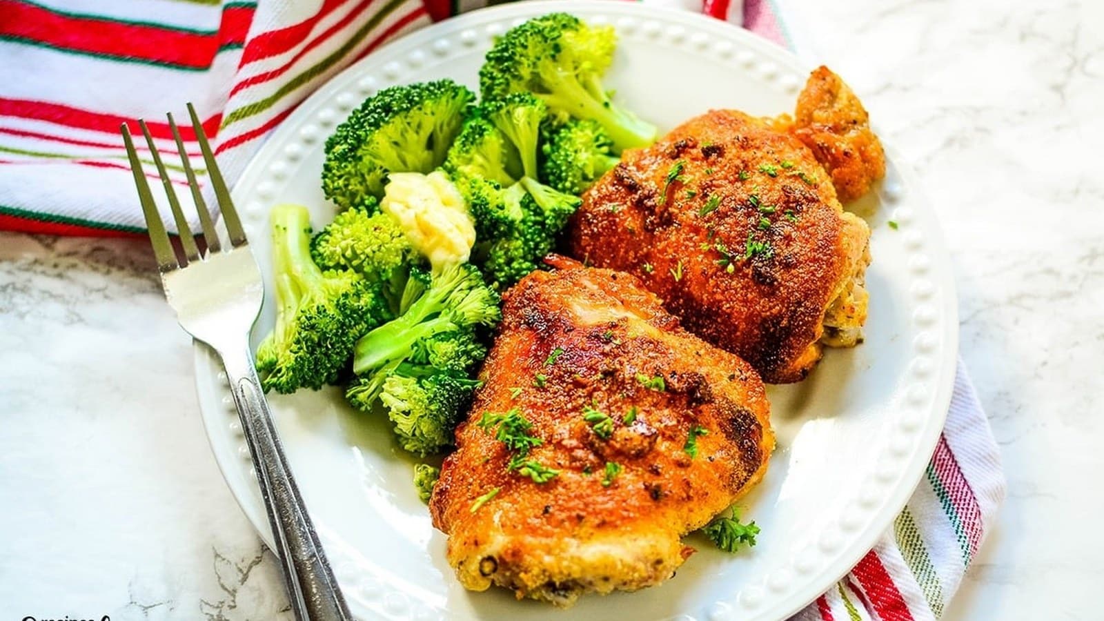 A plate with two pieces of seasoned, cooked chicken and steamed broccoli, accompanied by a fork on the side.