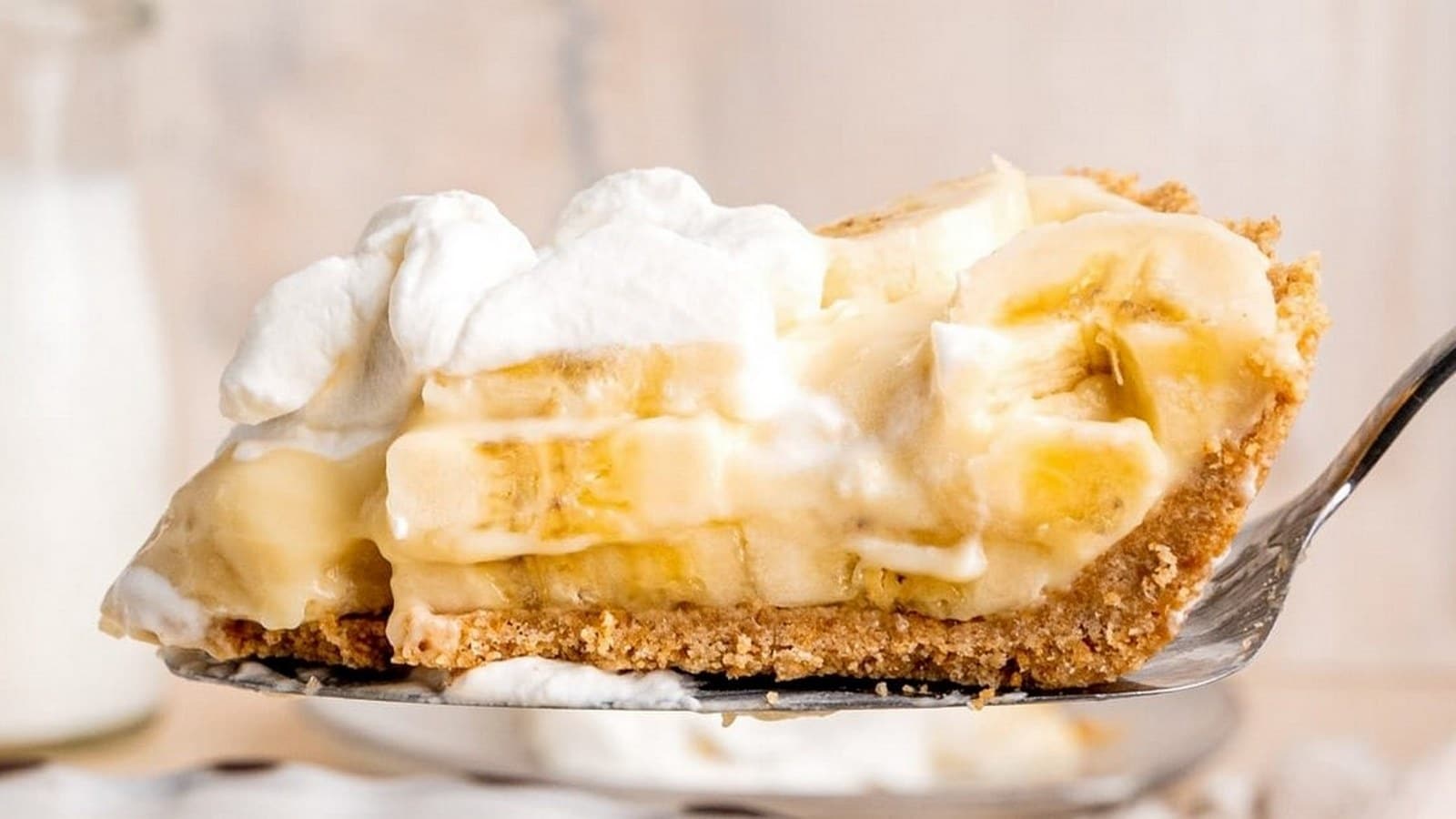 A slice of banana cream pie with whipped cream on a metal server.