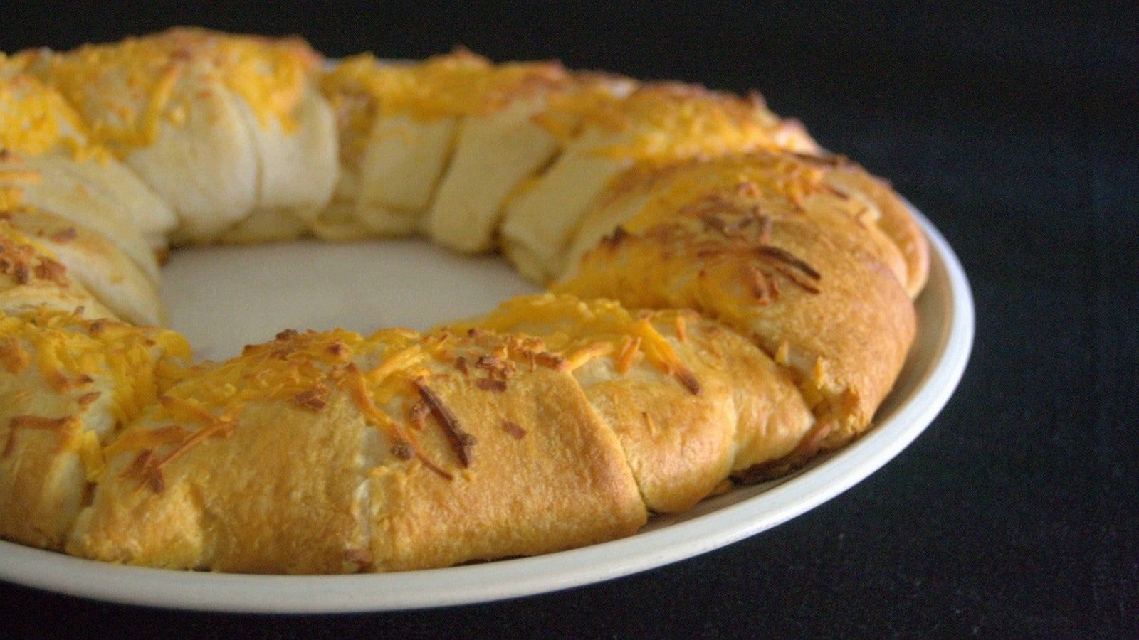 A circular, golden-brown baked bread topped with melted cheese on a white plate against a black background.