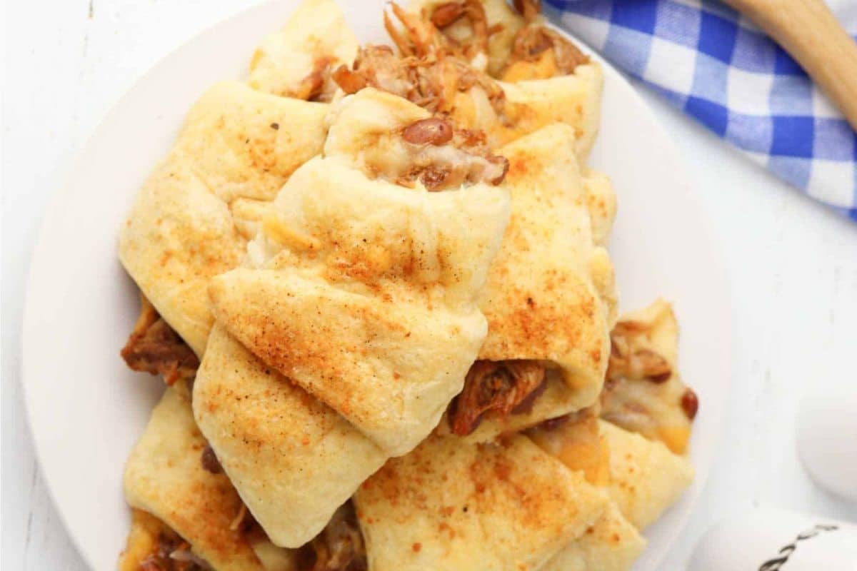 A plate of crescent rolls filled with shredded meat and cheese, sprinkled with seasoning. A blue and white checkered cloth is in the background.