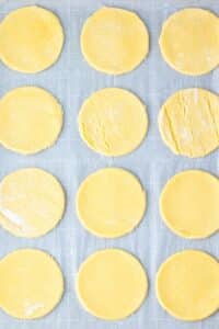 Twelve circular dough pieces arranged on a baking sheet with a light dusting of flour.