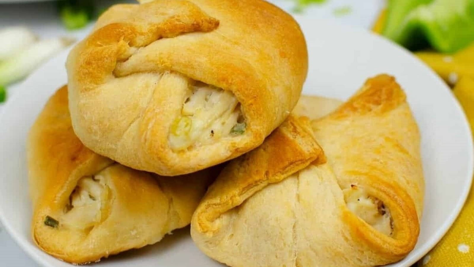 Three baked crescent rolls on a white plate, filled with a creamy mixture.