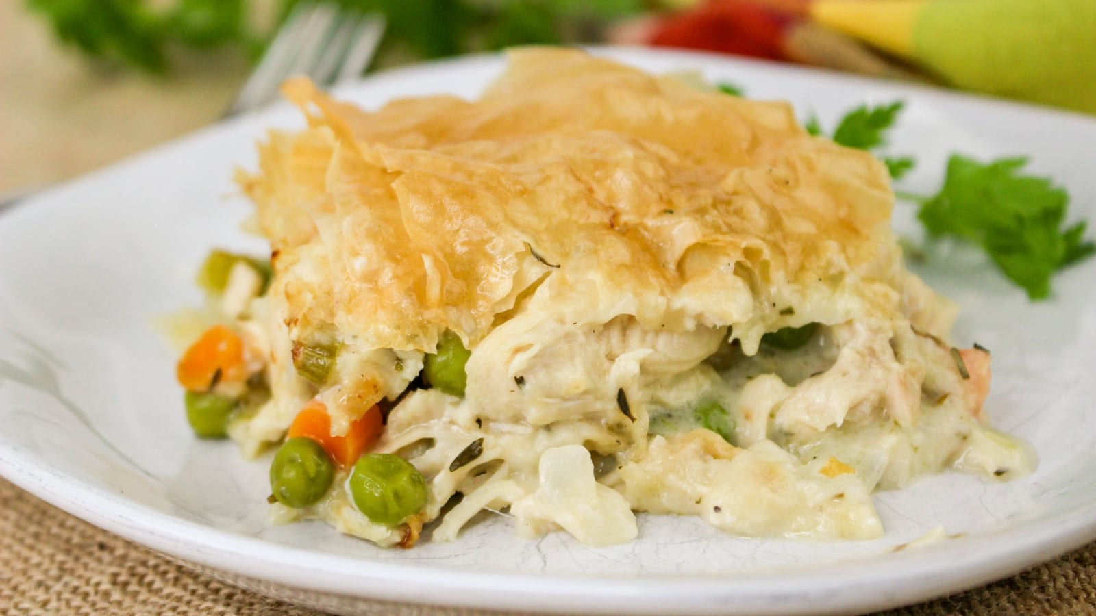 A slice of vegetable pot pie with a flaky crust served on a white plate, containing peas, carrots, and a creamy filling.