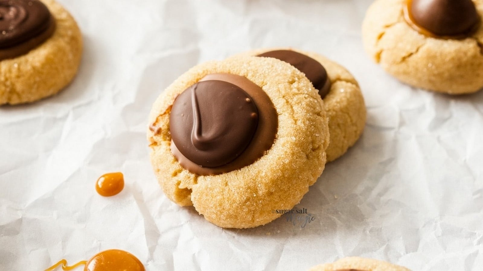 Two thumbprint cookies with chocolate centers on crumpled parchment paper.