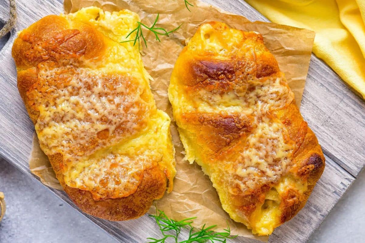 Two cheese-filled pastries on parchment paper, garnished with sprigs of dill, placed on a wooden surface.