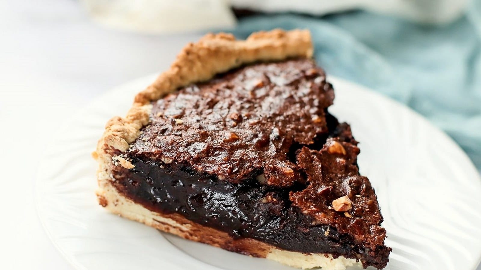 A slice of chocolate pie with a golden crust on a white plate, featuring a rich, gooey filling and a textured top.