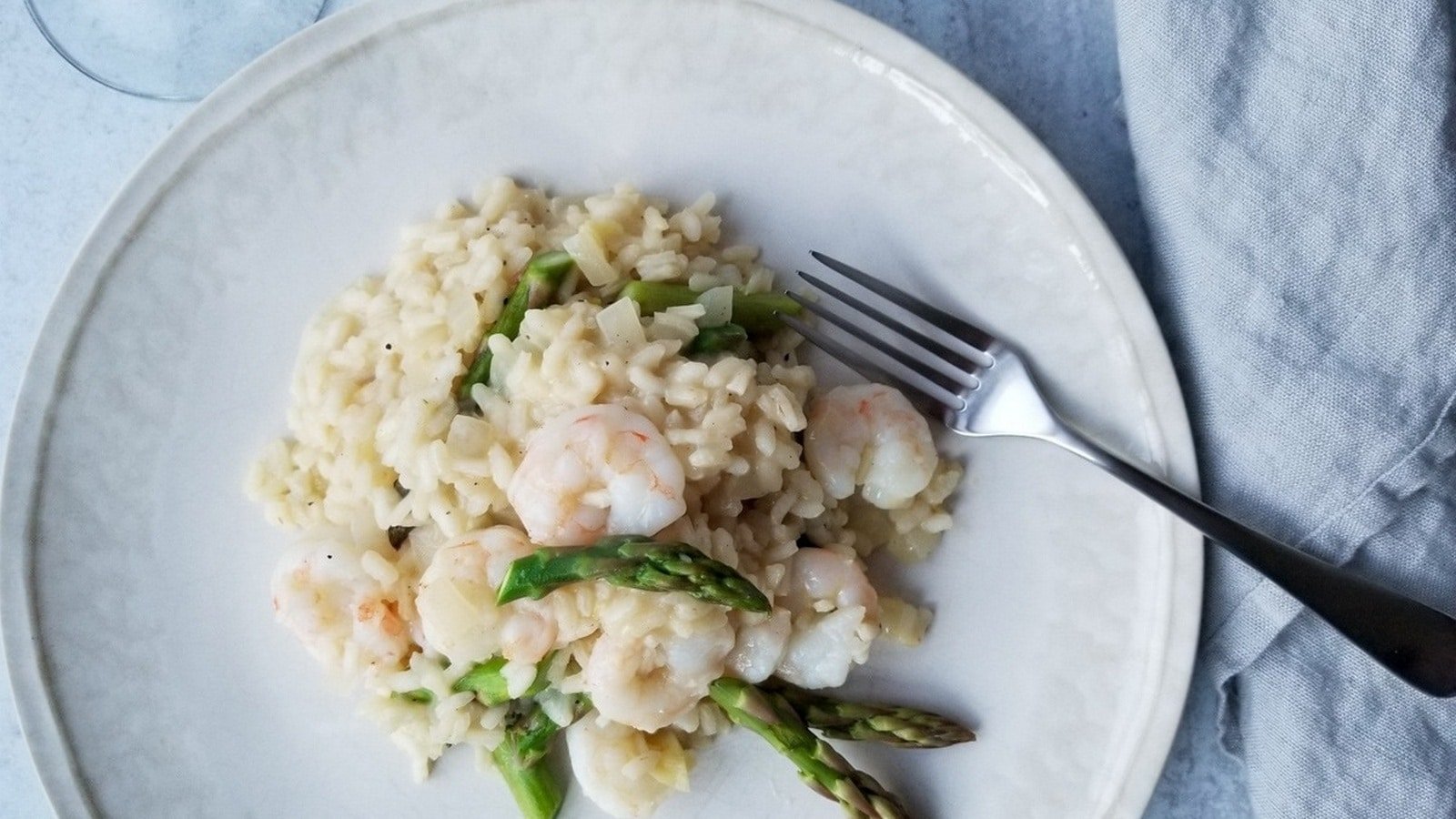 A plate of shrimp risotto with asparagus, accompanied by a fork on the side.