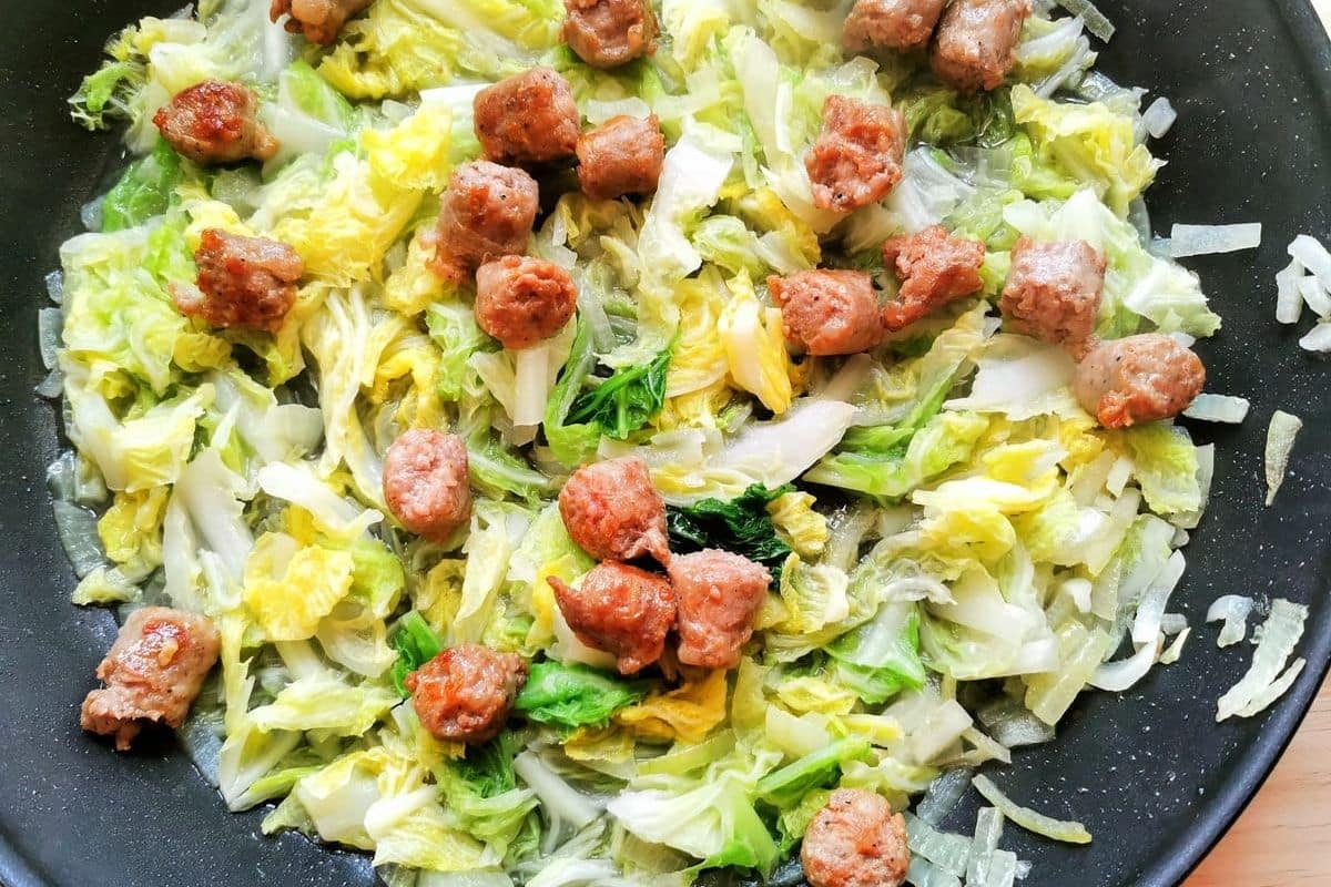 Cooked cabbage and sausage pieces in a pan.