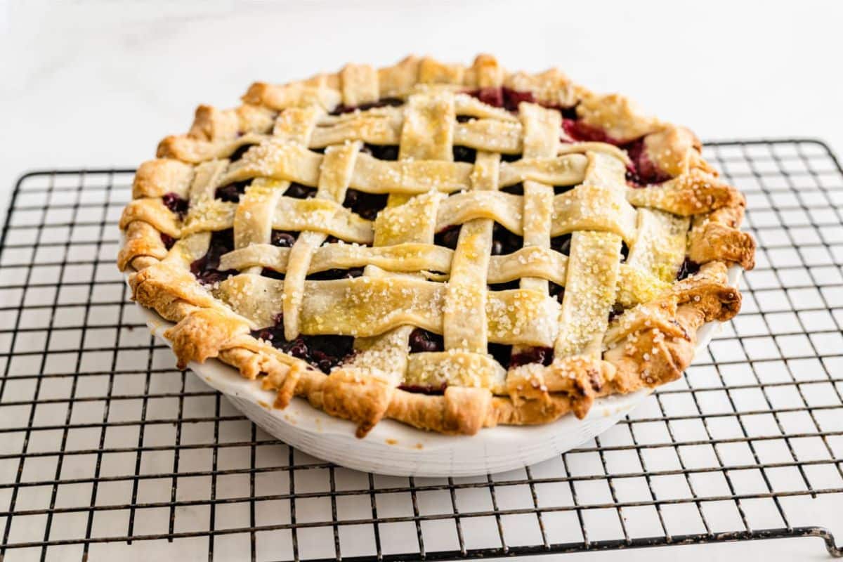 A freshly baked pie with lattice crust, sprinkled with sugar, sits on a cooling rack.