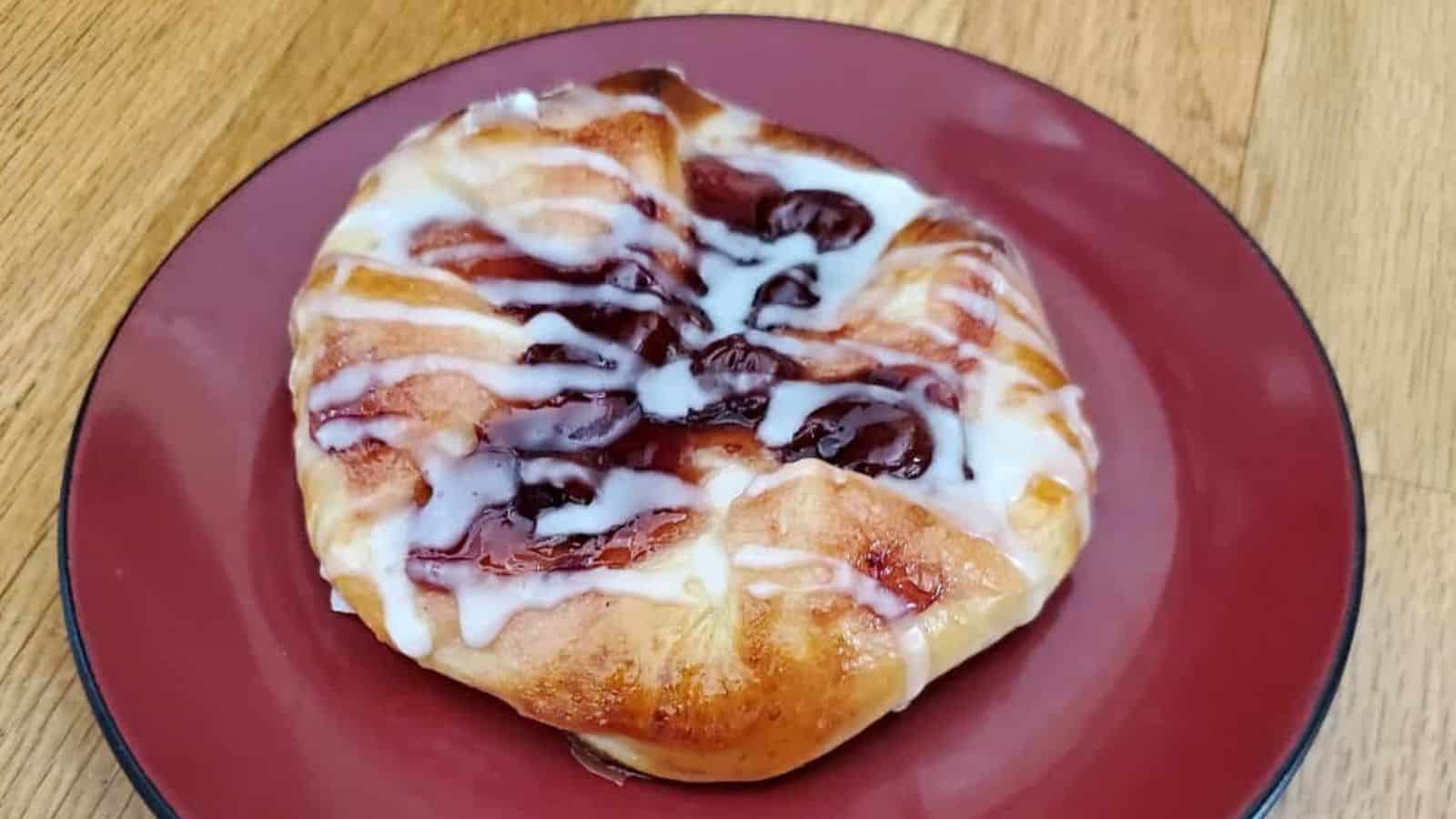 Pastry on a red plate with icing and fruit filling, placed on a wooden surface.