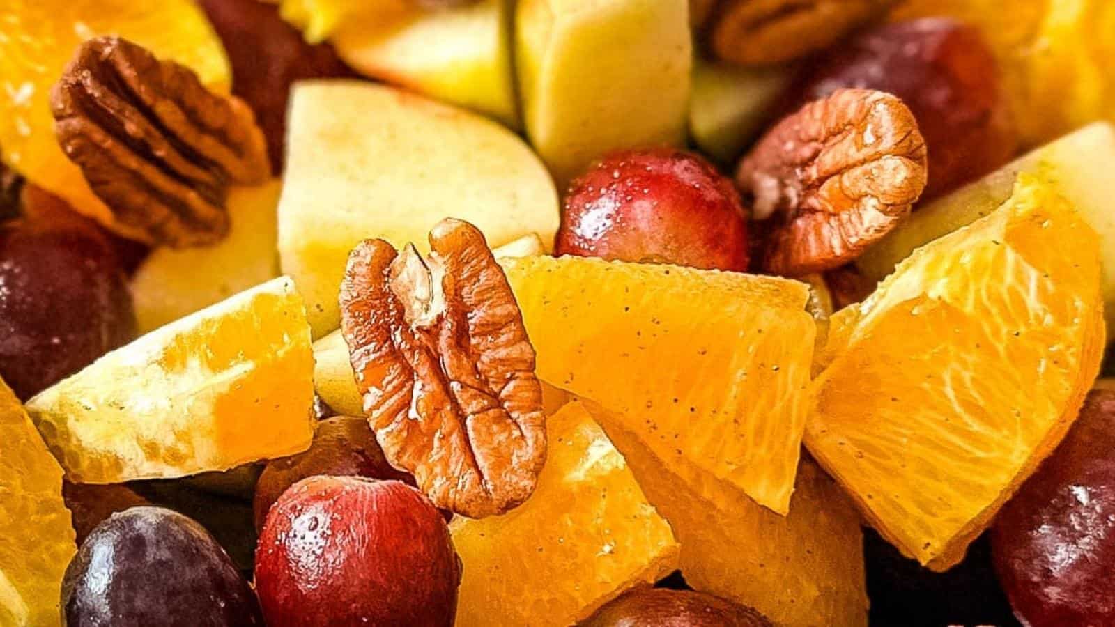 Close-up of a fruit salad with orange segments, apple pieces, grapes, and pecans.