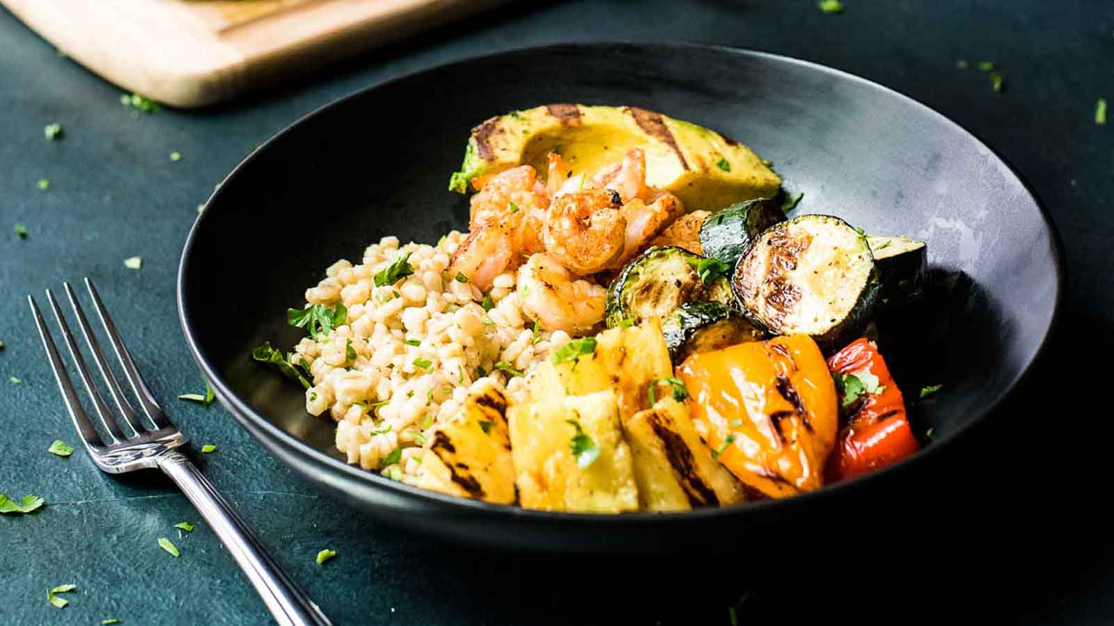 Overhead shot of shrimp skewers and veggie skewers next to a bowl of dressed grains.