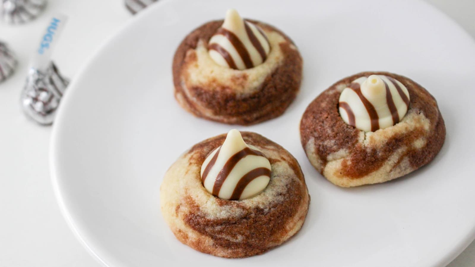 Three marbled cookies with striped chocolate and vanilla kisses on a white plate.