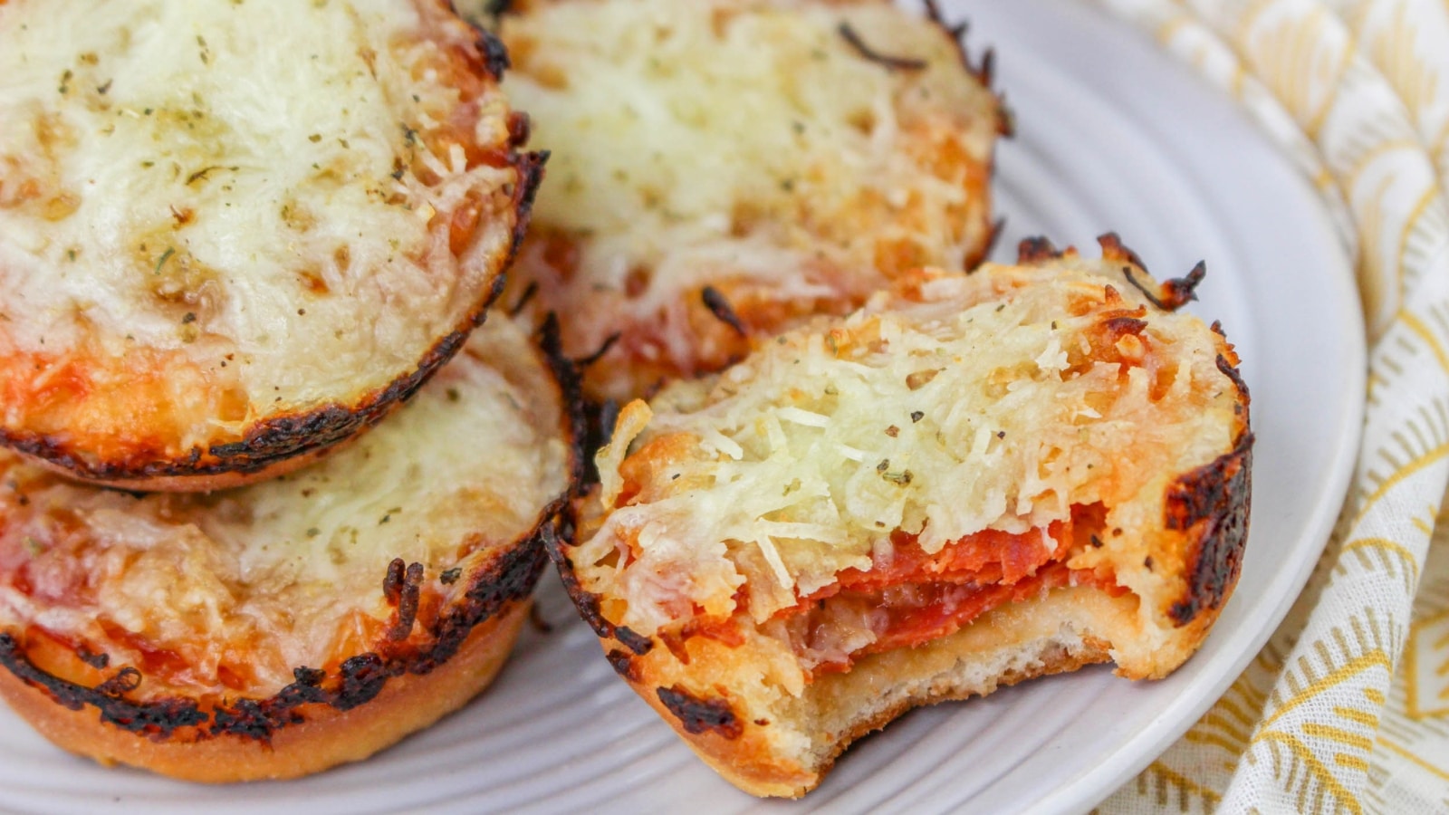 Mini pizzas with melted cheese and tomato sauce on a plate, one with a bite taken out.