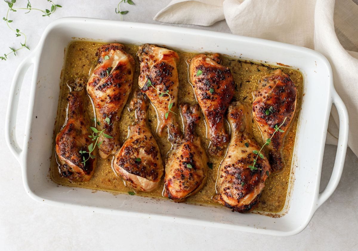 Slow-cooked chicken drumsticks in honey mustard sauce in a rectangular white baking dish.