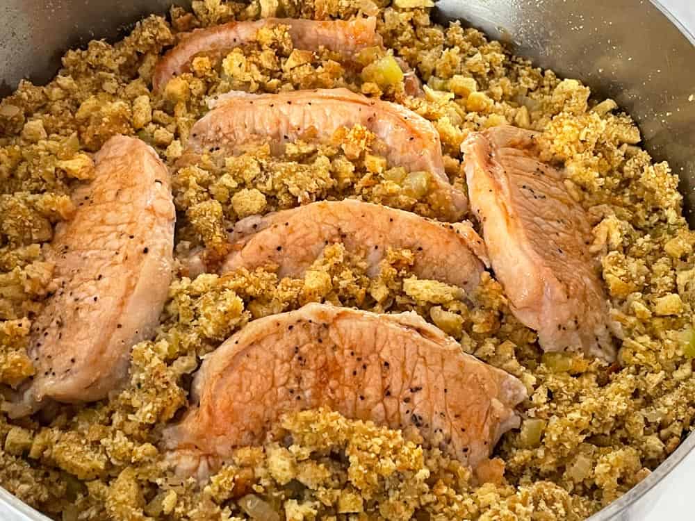 Pork chops seasoned with pepper, nestled in a bed of stuffing in a round dish.