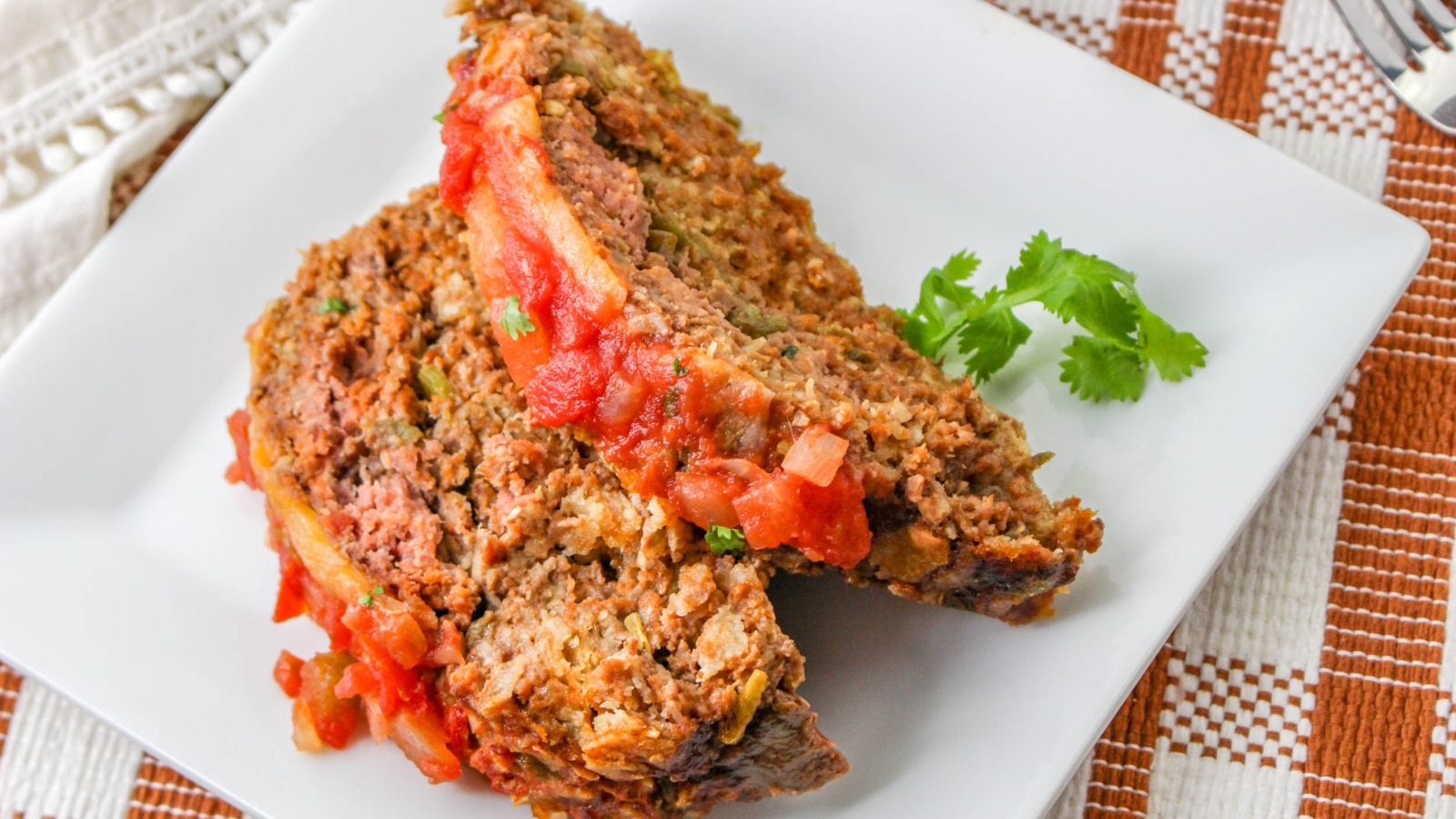 Two slices of meatloaf topped with tomato sauce on a white plate, garnished with a sprig of cilantro.