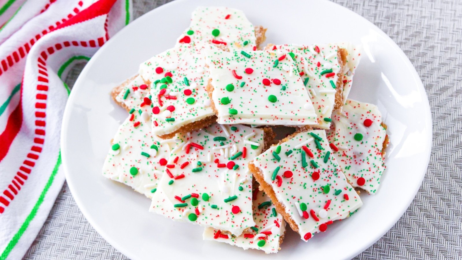 A plate of white chocolate bark topped with red, green, and white sprinkles, placed on a woven surface.