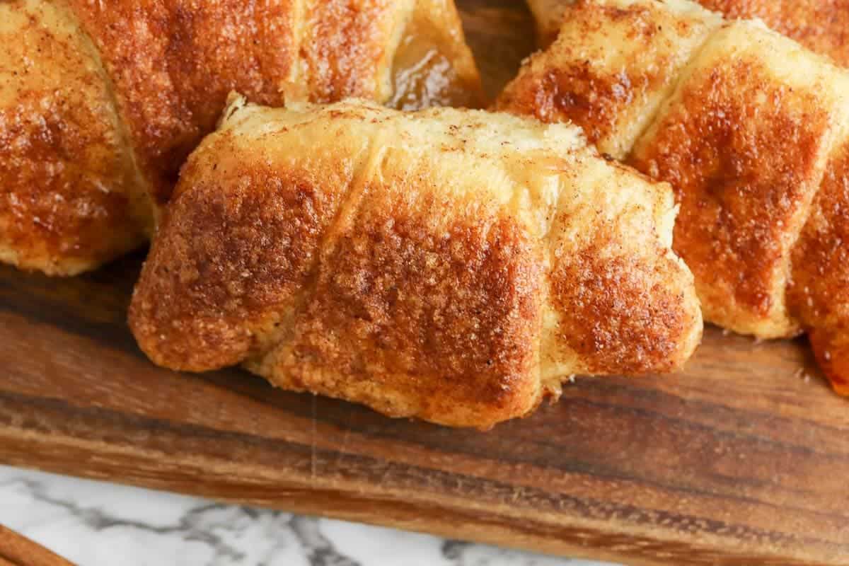 Close-up of two golden-brown croissants on a wooden surface, showing a flaky texture with cinnamon sugar sprinkled on top.