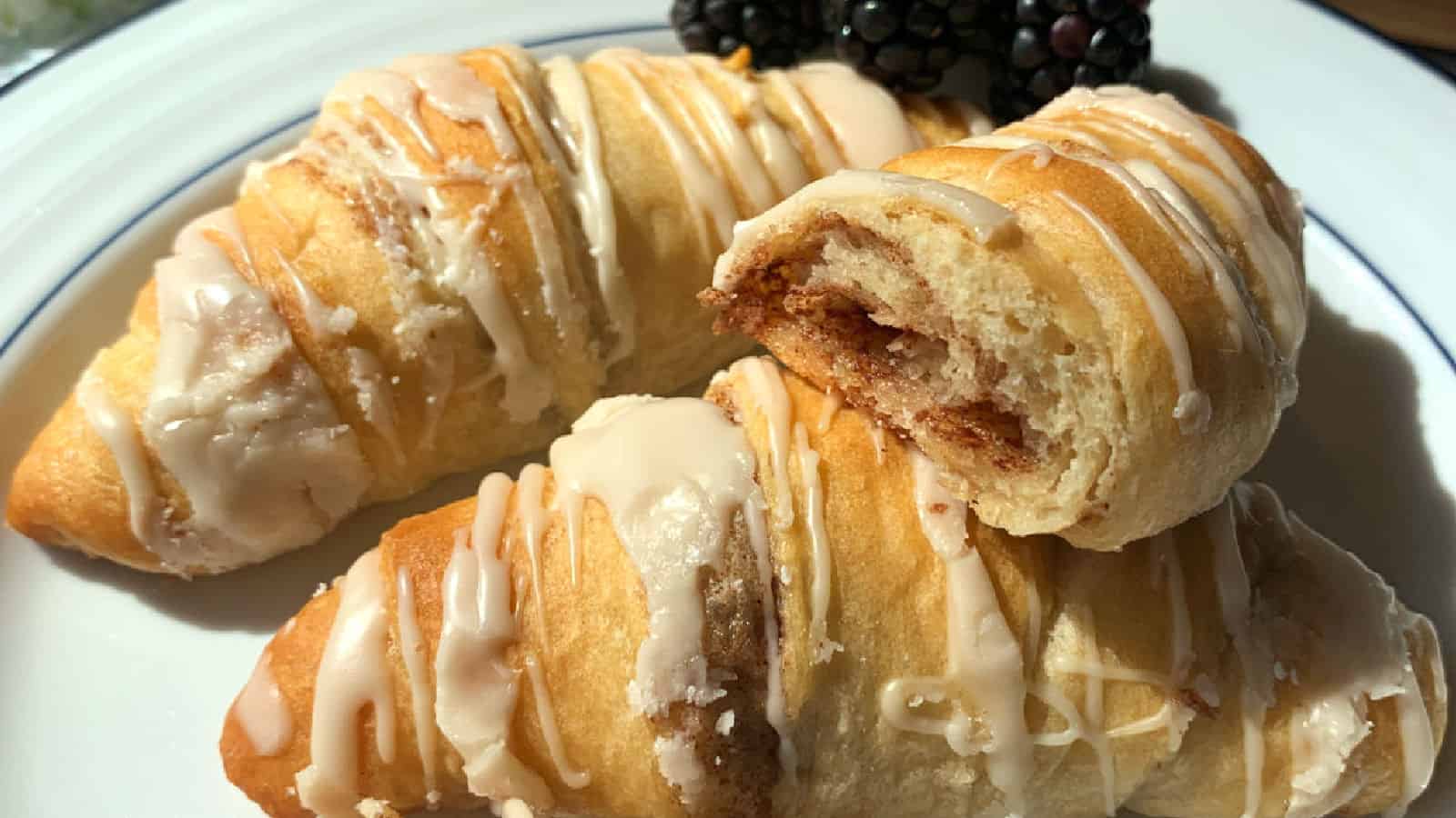 Three glazed croissants on a white plate with blackberries in the background.