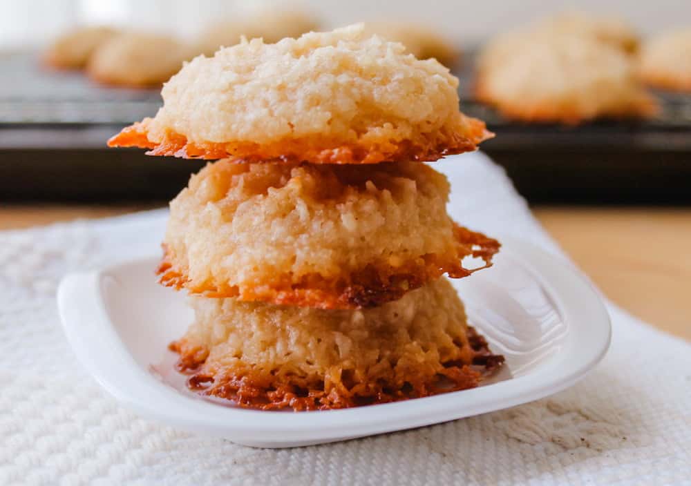Three coconut macaroons stacked on a small white plate, with a baking tray in the background.