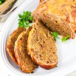Sliced meatloaf on a white plate, garnished with parsley.