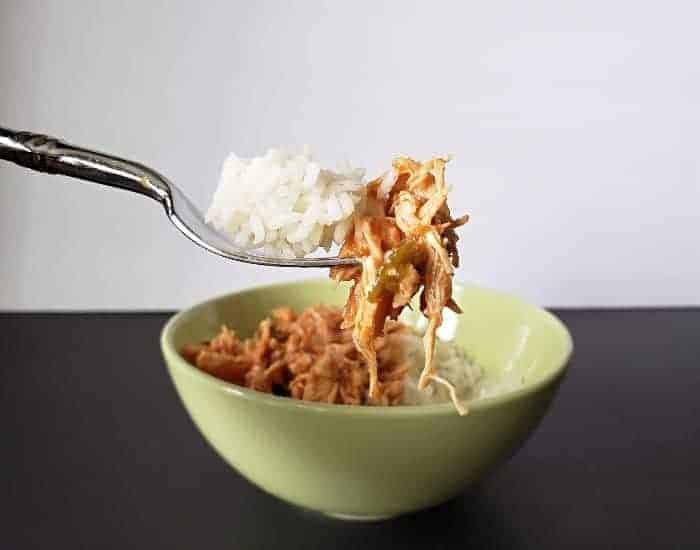 Image shows a Bite of tomato lime chicken on a fork with rice and the rest of the bowl in the background.