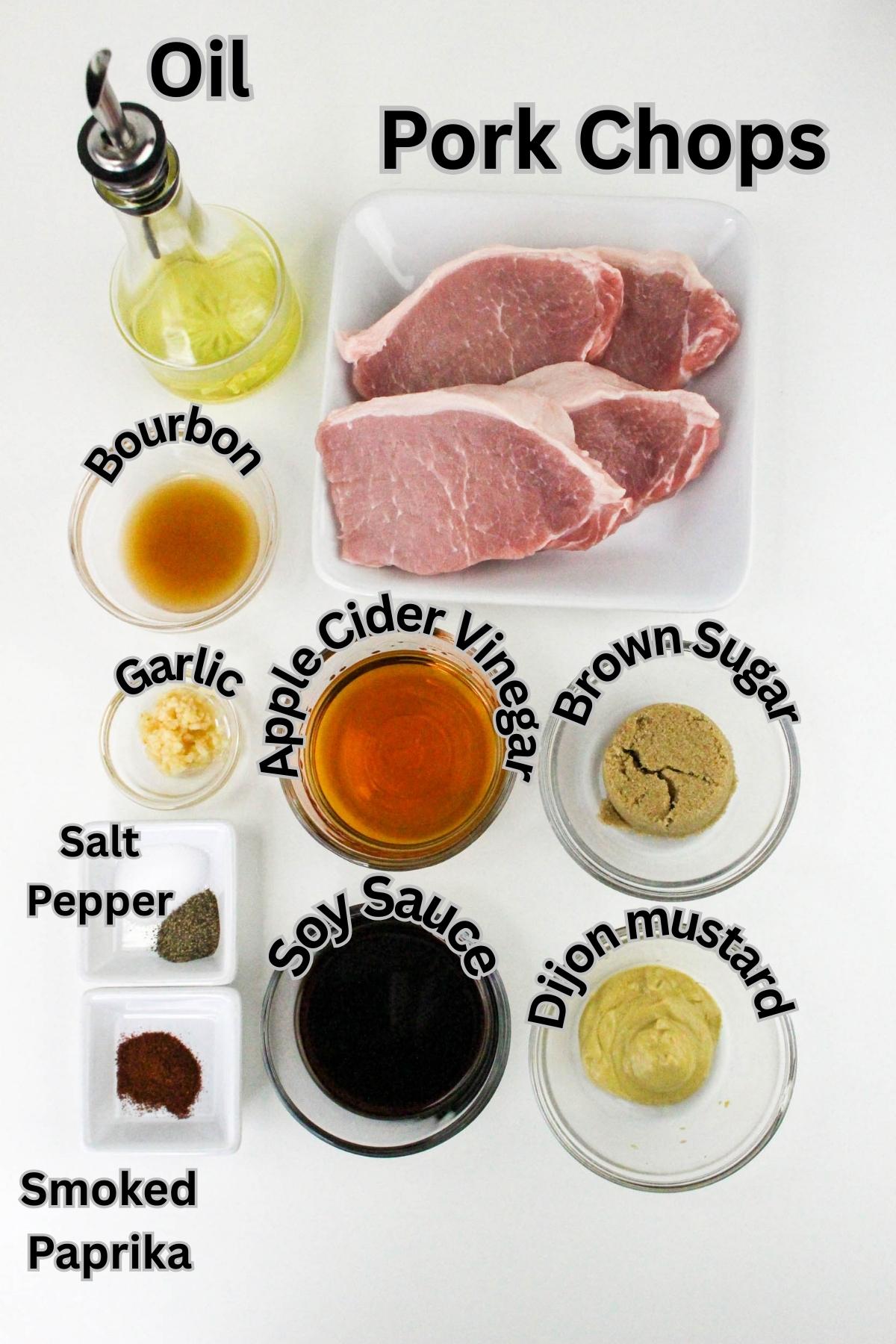 Overhead view of ingredients for pork chops including oil, bourbon, garlic, apple cider vinegar, brown sugar, salt, pepper, soy sauce, Dijon mustard, and smoked paprika.
