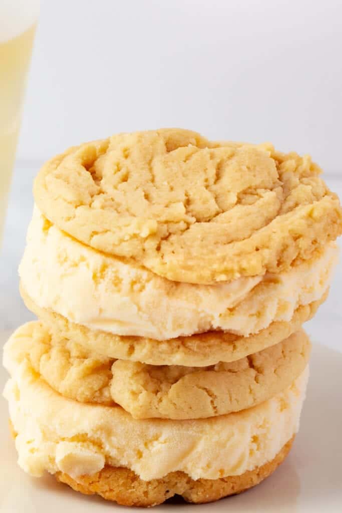 A stack of three ice cream sandwiches made with vanilla ice cream between two round, golden cookies on a white surface—a delightful treat to pair with your favorite peach recipe ideas.