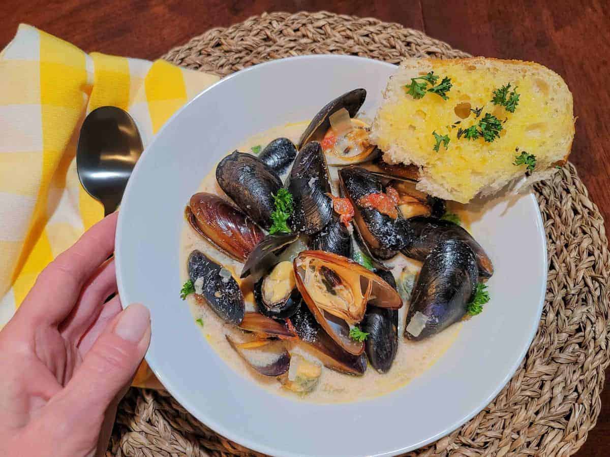 A person holding a bowl of steamed mussels.