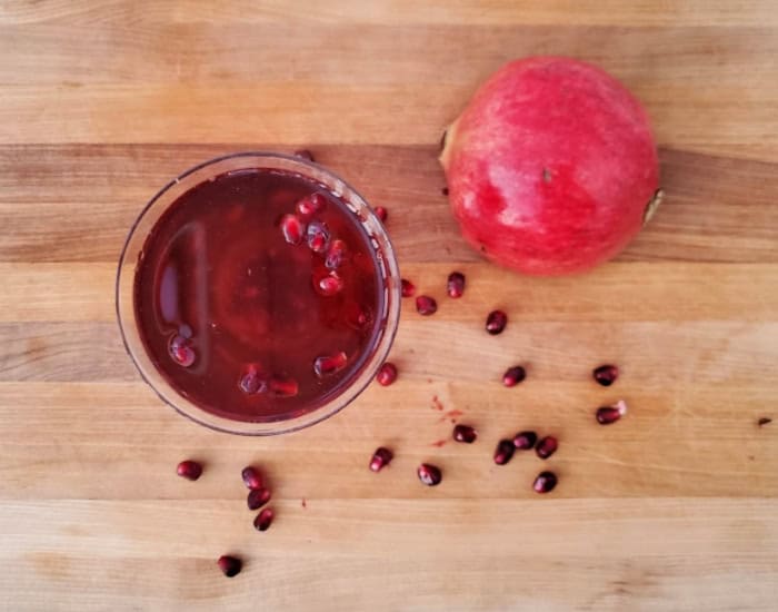 Image shows a martini glass with a Pomegranate Fizz Cocktail and pomegranate arils around it.
