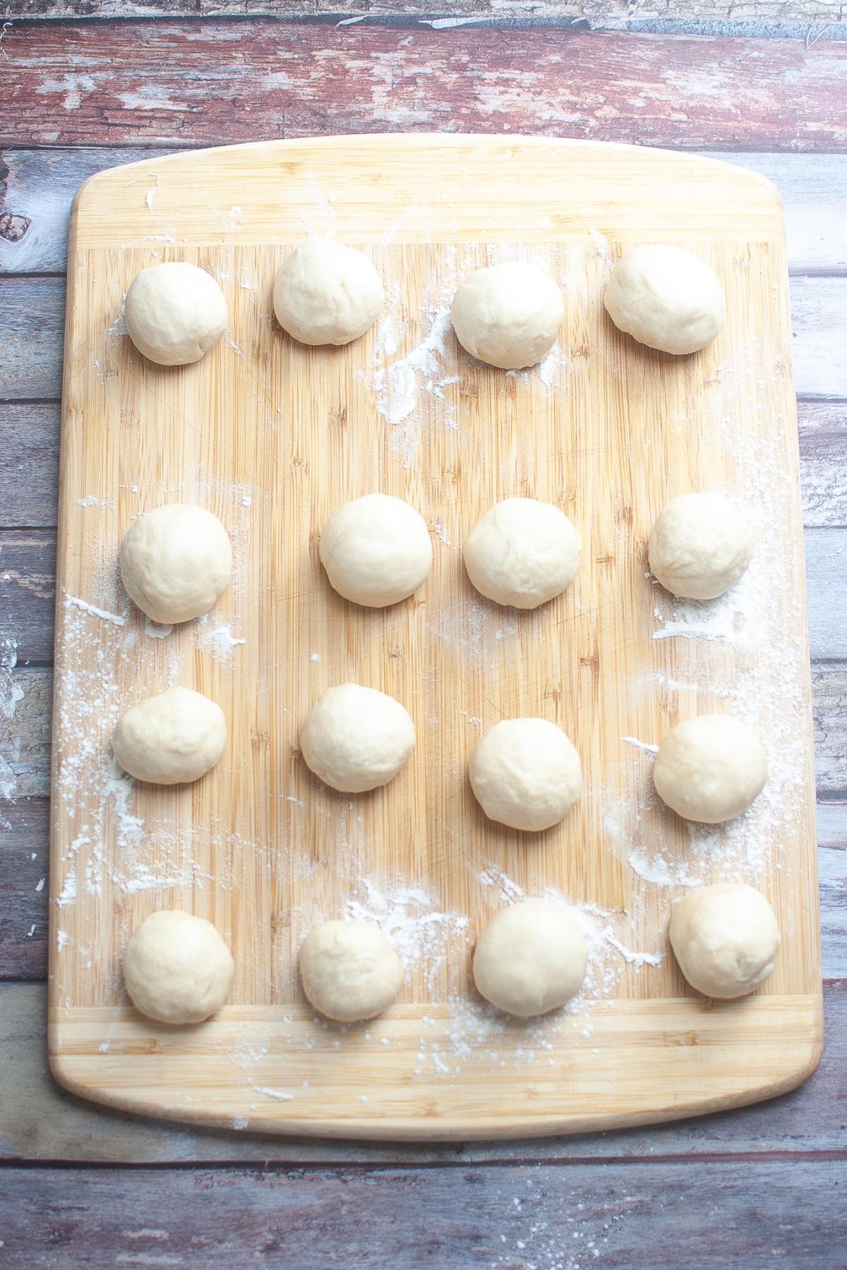 A wooden board with fifteen evenly spaced dough balls on a lightly floured surface.